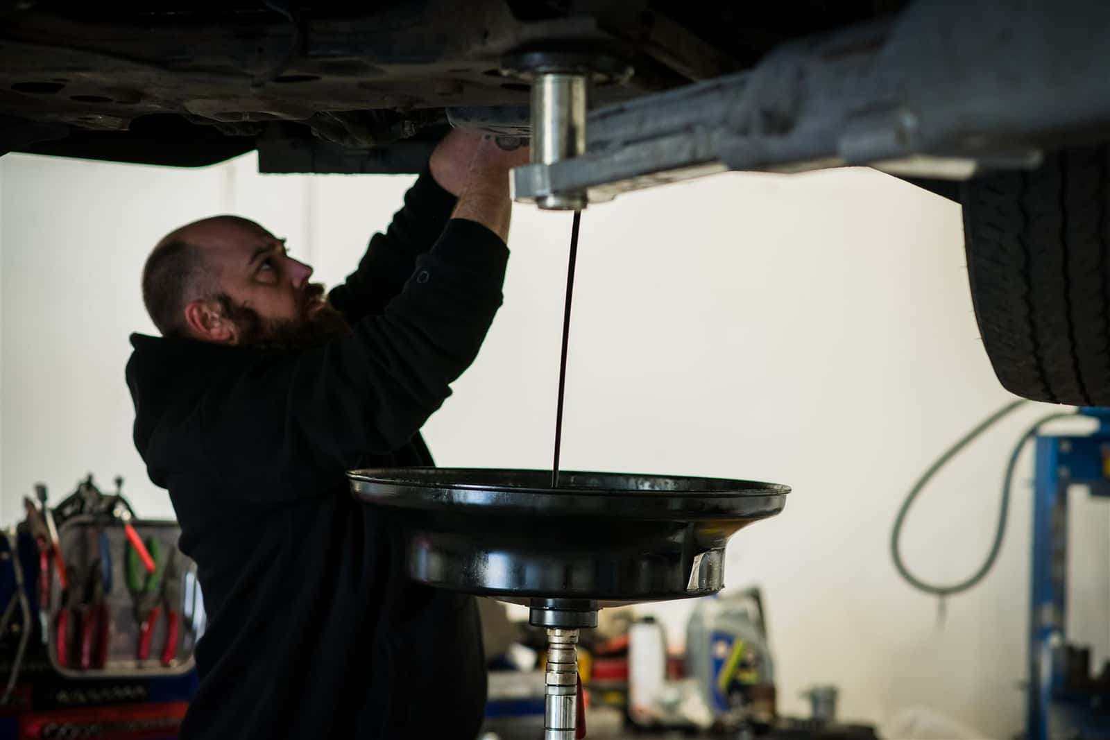 A technician draining used engine oil from a car into a catch tray during a service